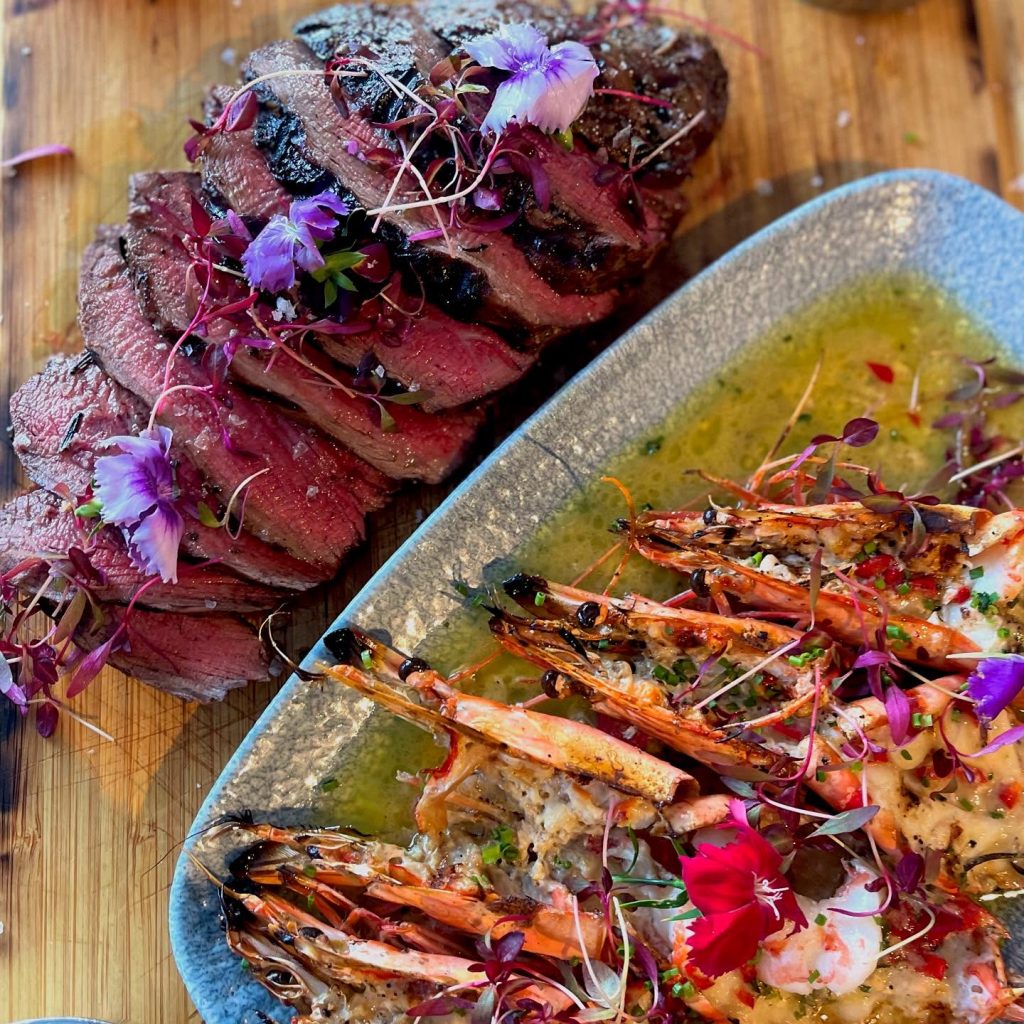 Platter of Italian fine dining at Pollino Restaurant in Halifax, featuring sliced medium-rare beef garnished with edible flowers alongside king prawns in garlic butter sauce.