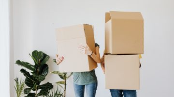 2 people holding boxes ahead of a house move