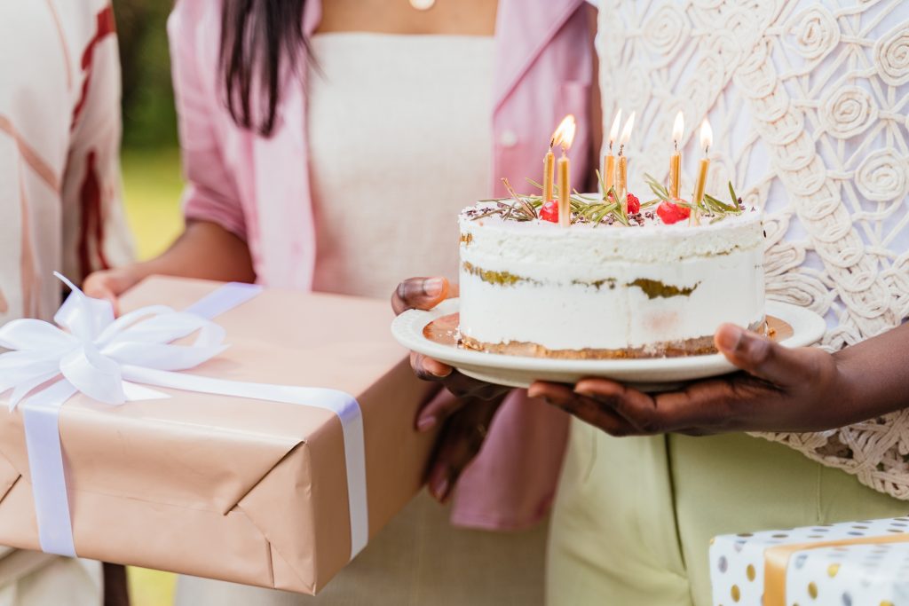 A beautifully decorated cake adorned with candles and surrounded by an assortment of thoughtful complimentary gifts, showcasing the essence of celebration and surprise.
