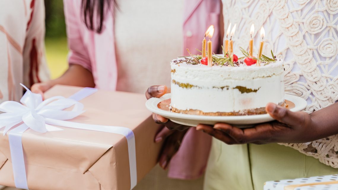 A beautifully decorated cake adorned with candles and surrounded by an assortment of thoughtful complimentary gifts, showcasing the essence of celebration and surprise.