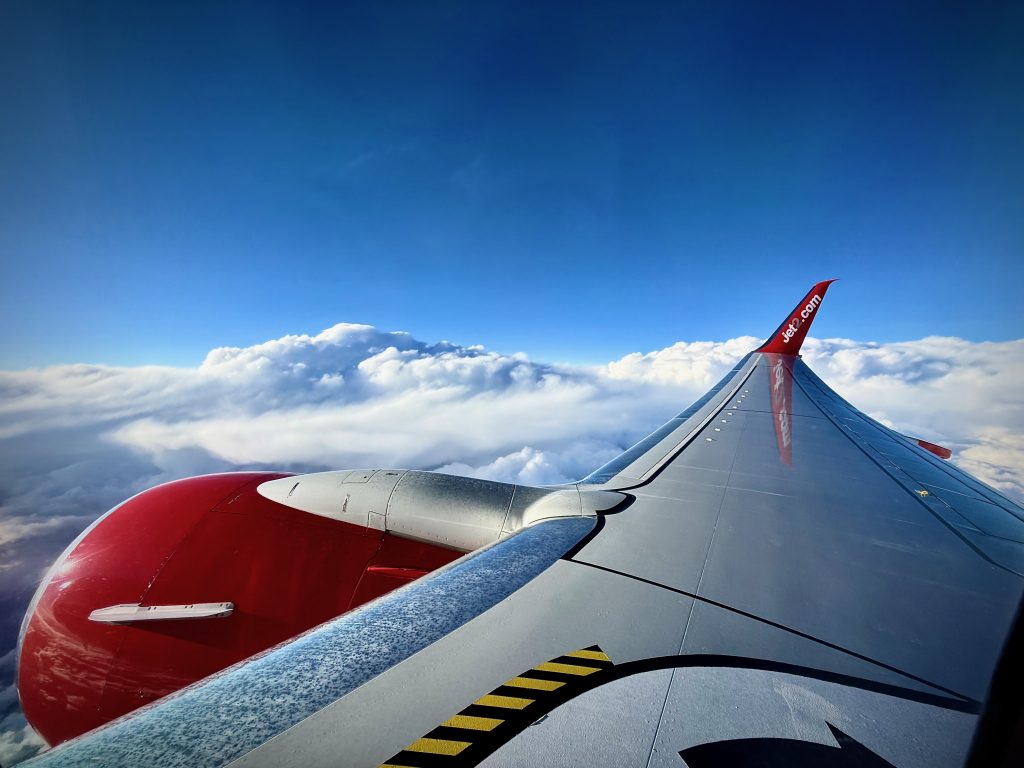 View from the Jet2 aircraft window showcasing a vibrant blue sky, fluffy white clouds, and the iconic red-tipped wing, capturing the serenity of the journey to Marrakech
