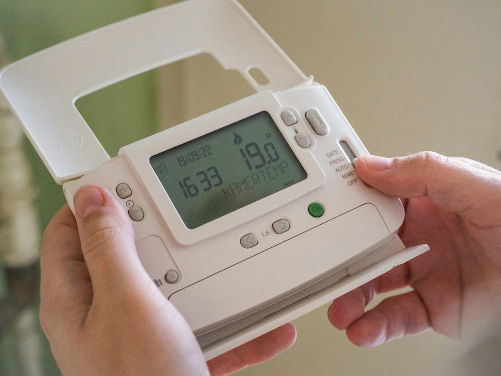 Close-up of hands adjusting the settings on a digital thermostat, highlighting temperature control and home energy management.