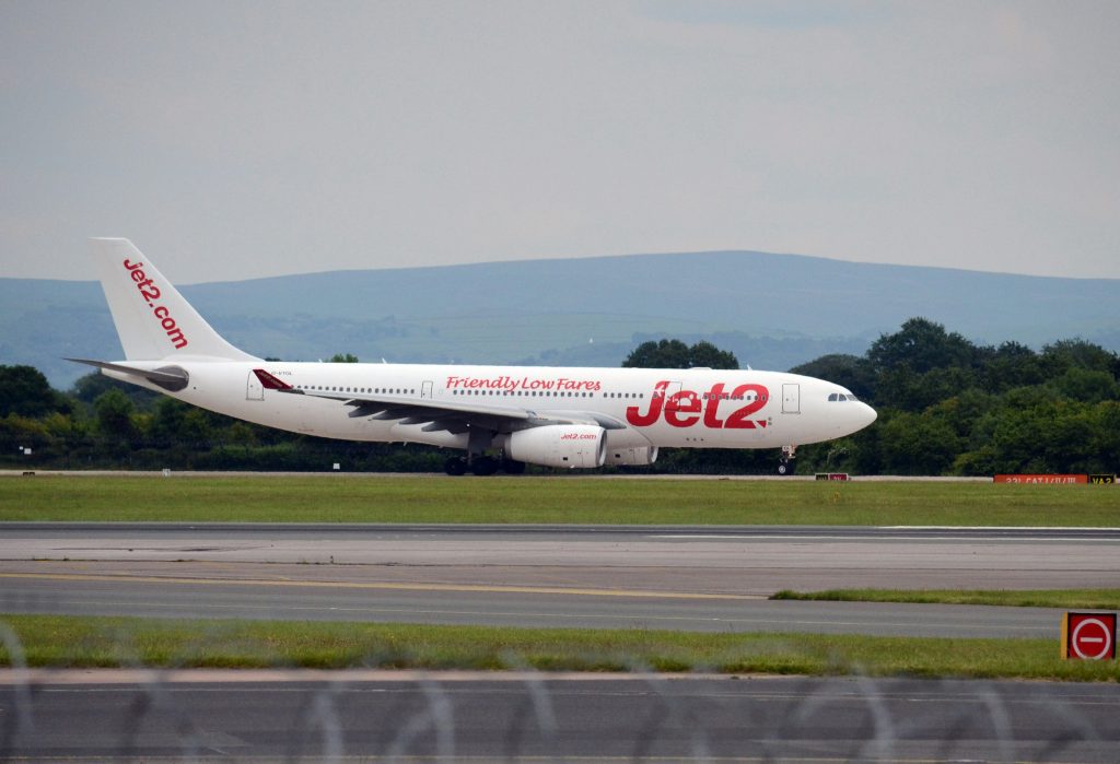 Jet2 plane on the runway at Manchester Airport, ready for departure, with scenic countryside in the background.