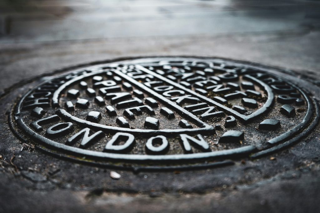 Close-up of a London manhole cover with intricate text and patterns, highlighting urban infrastructure.