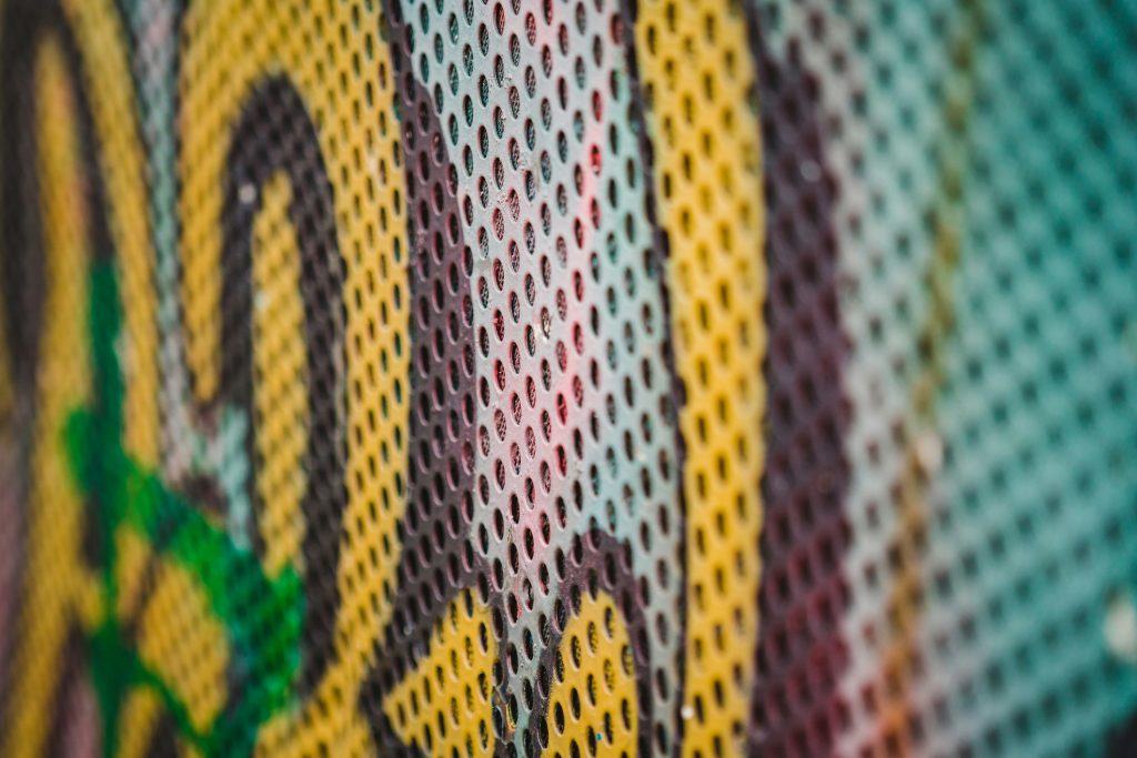 Close-up of a colourful metal mesh with graffiti-style designs featuring green, yellow, and red patterns.
