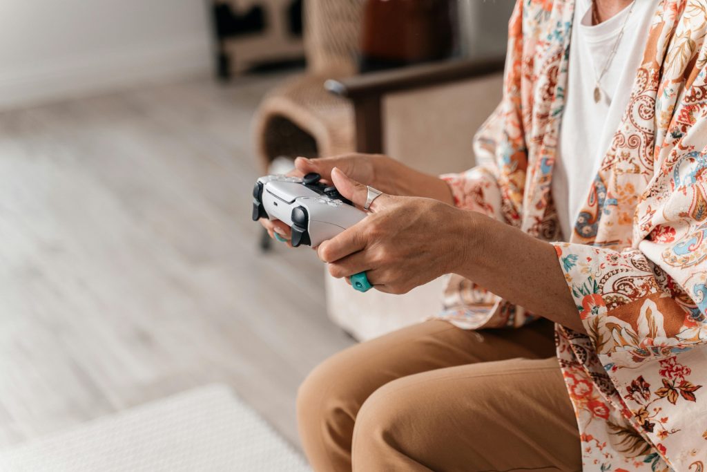 Person holding a video game controller, seated in a cozy living room with bright natural lighting and a casual, relaxed atmosphere.