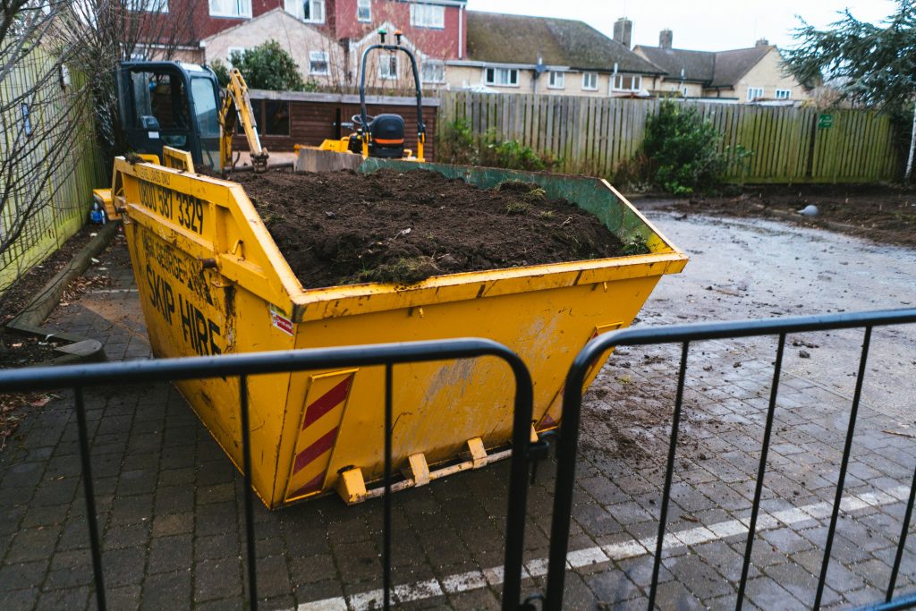Yellow skip bin filled with soil at a residential site, highlighting efficient waste management and skip hire solutions.