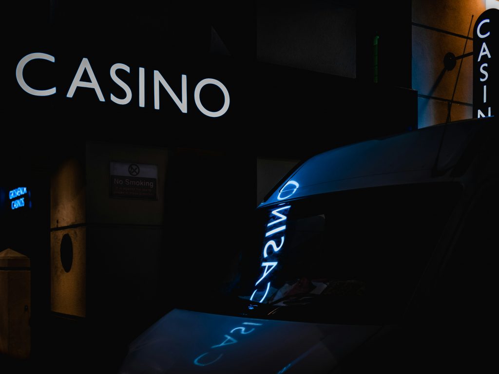 Neon-lit casino sign reflecting off a car window at night, creating a moody and atmospheric scene.