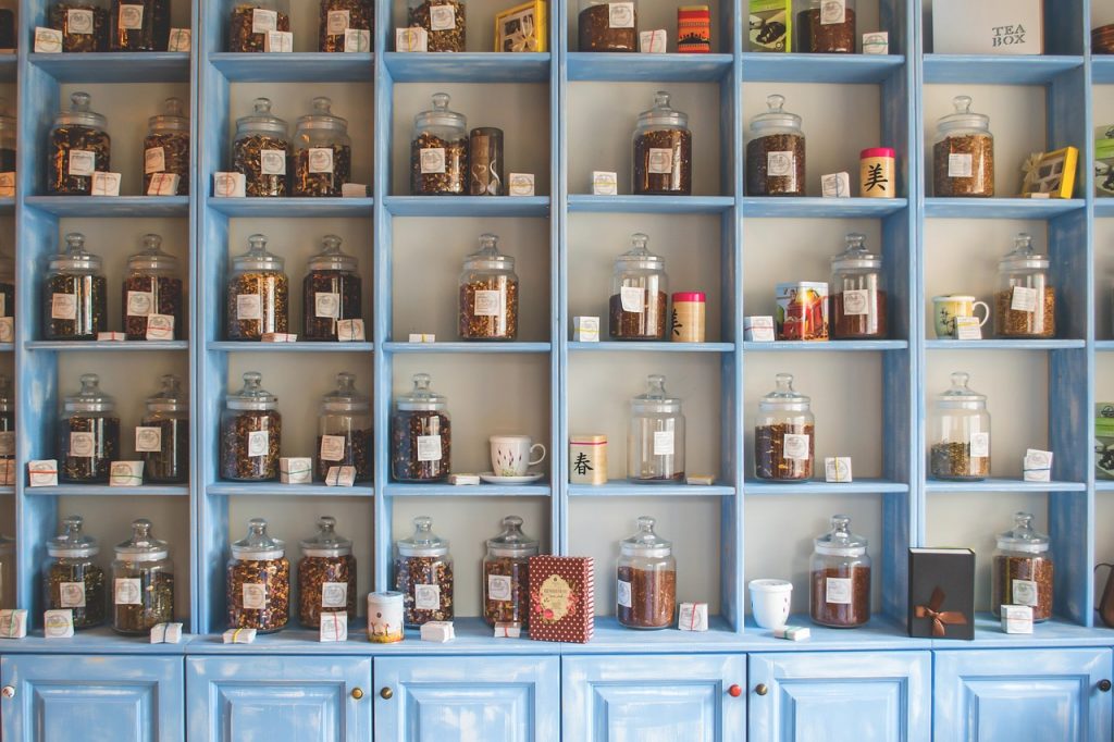 A neatly arranged display of glass jars filled with herbal tea and spices on pastel blue wooden shelves, creating a charming and organized apothecary-style setting.