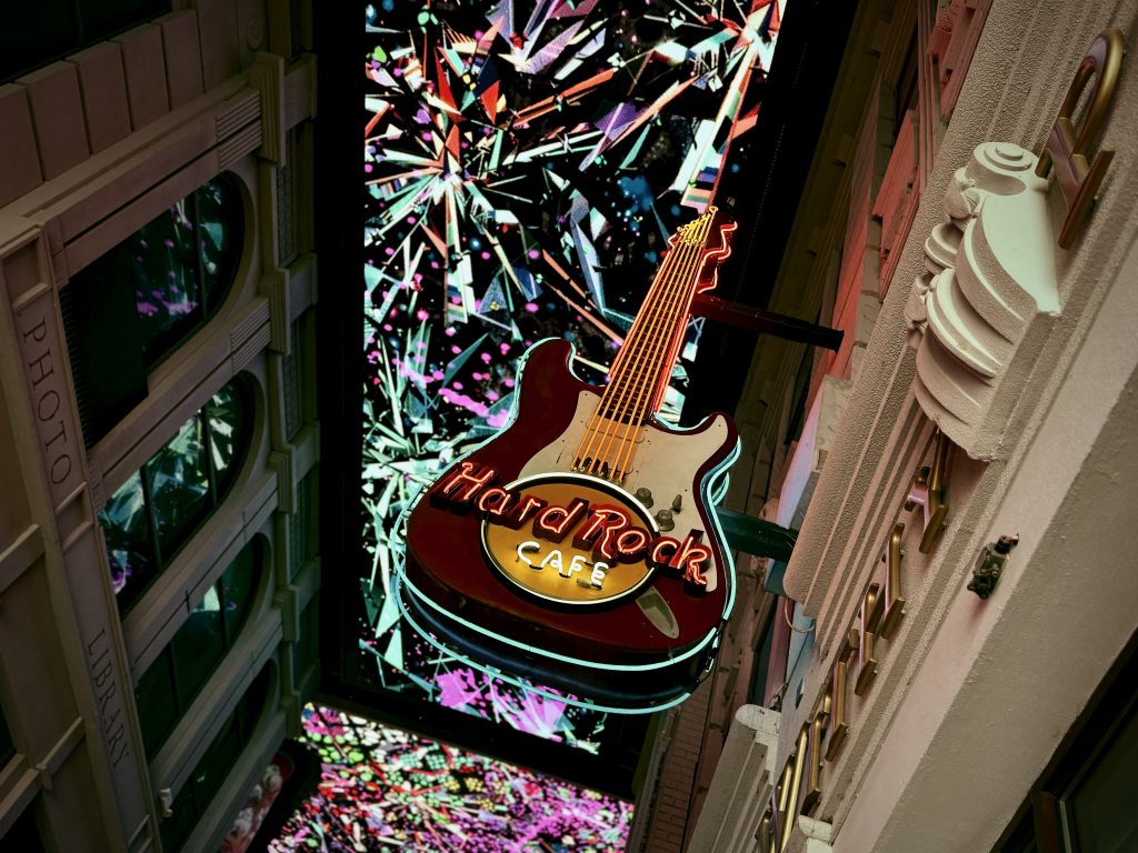 Illuminated Hard Rock Cafe guitar sign against a vibrant, abstract backdrop of colourful neon lights, captured at night in Manchester’s city centre.