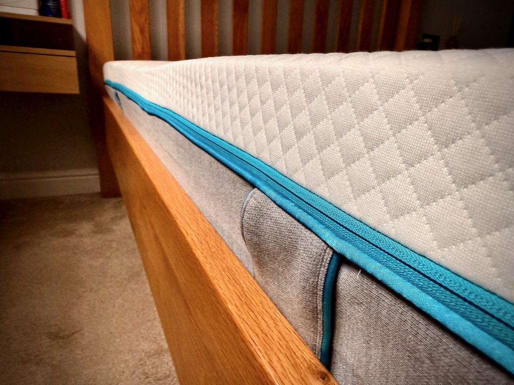 Close-up view of the Simba Hybrid Original Mattress showing the quilted top layer and signature blue trim on a wooden bed frame.