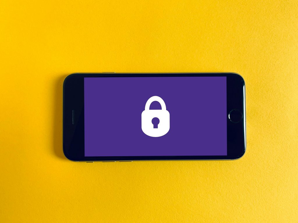 A smartphone lying on a yellow surface displays a purple screen with a white padlock icon, symbolizing digital security or secure login.