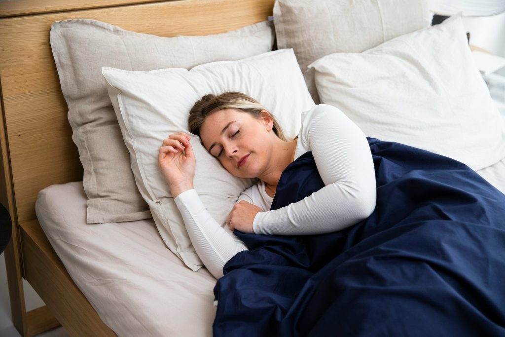 Young woman peacefully sleeping in a cosy bed with white pillows and a navy blue duvet