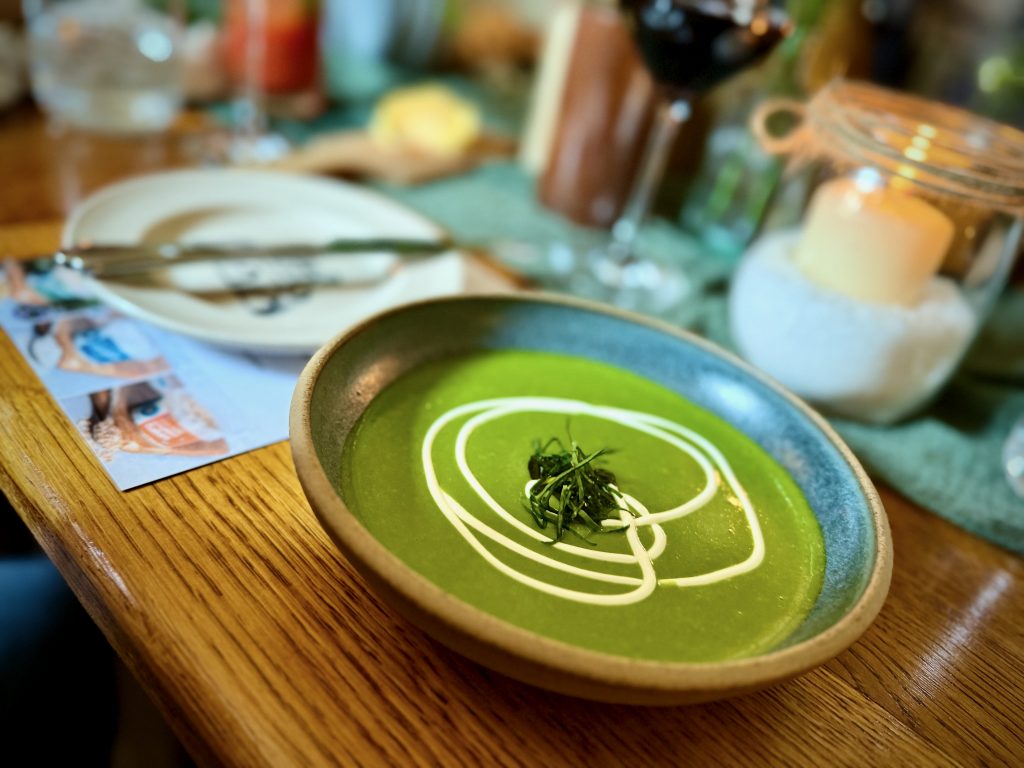 Vibrant wild garlic soup garnished with a swirl of cream and fresh herbs, served at The Abbey Inn with Cornish Sea Salt branding visible on the table