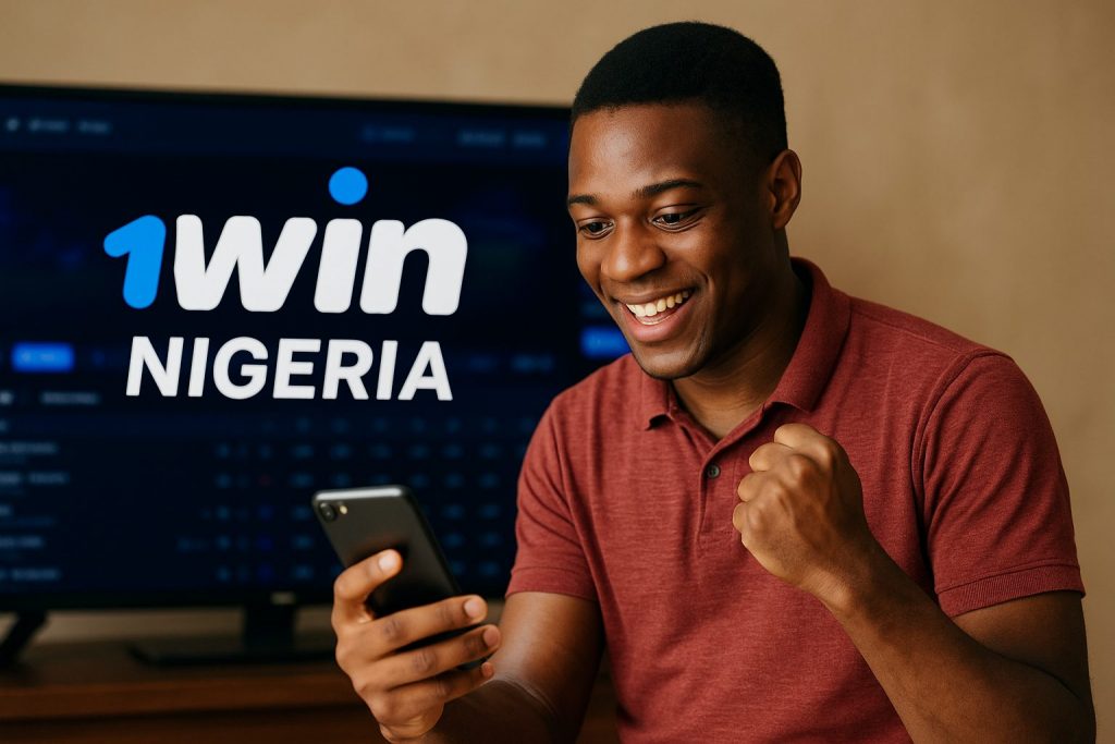 A young Nigerian man wearing a red polo shirt smiles excitedly while looking at his smartphone, holding it in one hand and clenching his other fist in celebration. Behind him, a TV screen displays the “1win Nigeria” logo with a blurred sports betting interface, creating a dynamic scene of online gaming and betting enthusiasm.