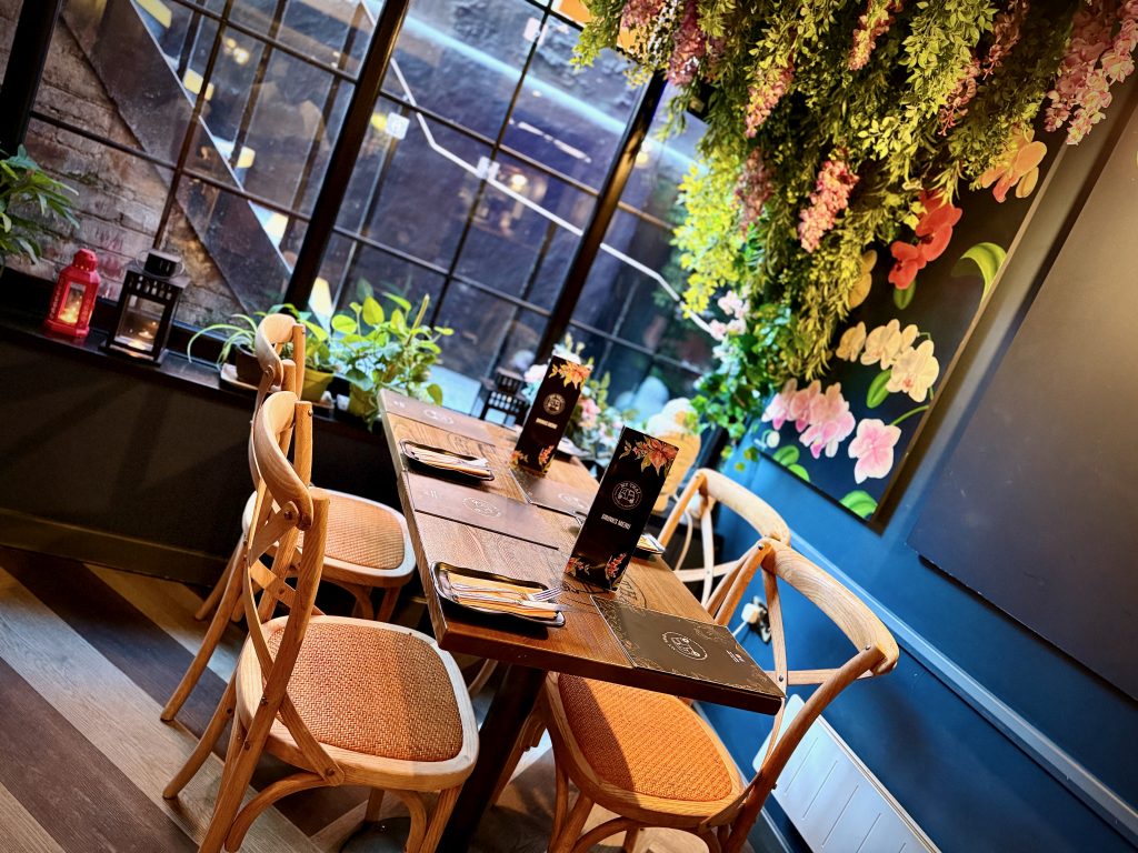 Cosy dining area at My Thai (Old Steps) in Leeds featuring wooden chairs, floral ceiling décor, and a large window with natural light.