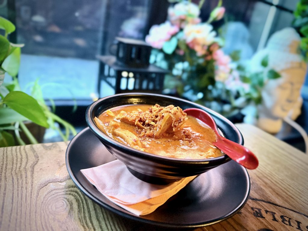 Bowl of rich chicken Massaman curry topped with crispy onions, served in a black bowl with a red spoon at My Thai (Old Steps) in Leeds.