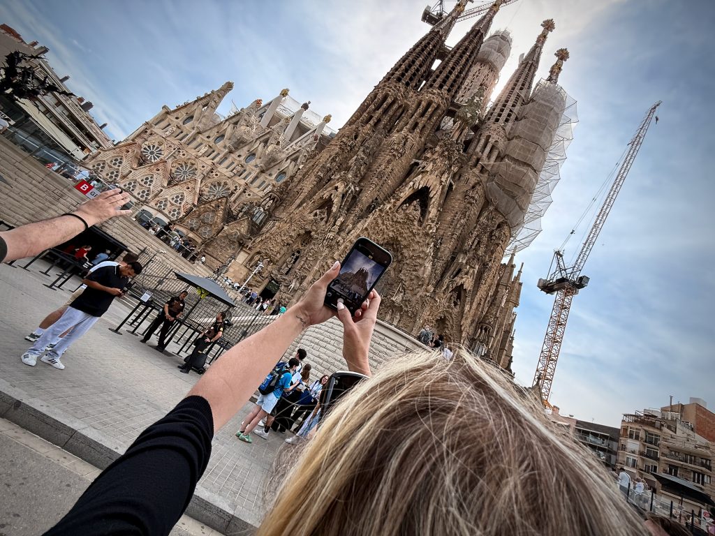 A visitor takes a photo of the iconic Sagrada Família in Barcelona, capturing the intricate gothic and modernist architecture of Antoni Gaudí’s masterpiece, with cranes towering above as construction continues.