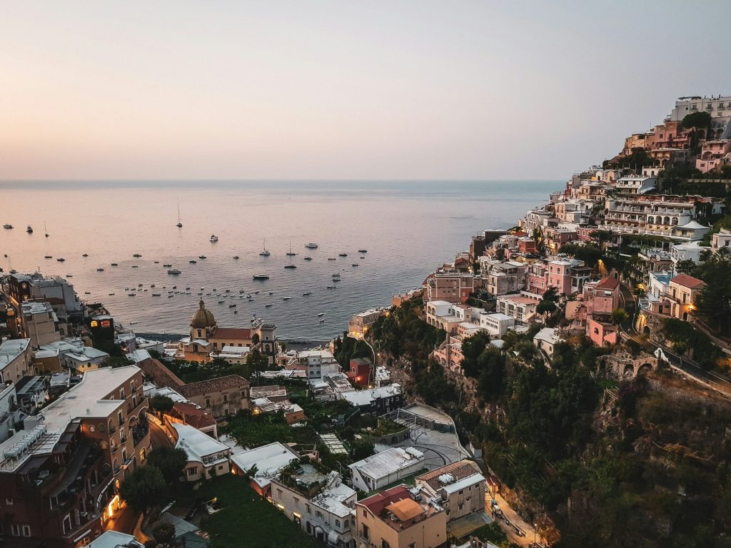 Sunset view of Positano on the Amalfi Coast, with pastel-coloured houses cascading down the hillside towards the sea, dotted with boats.
