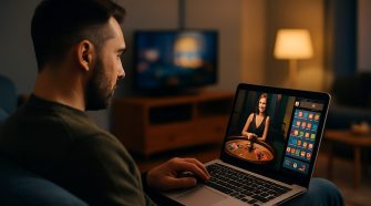 A man sits on a modern sofa in a dimly lit living room, focused on a laptop displaying a live online casino game with a female dealer and poker chips. A television and warm ambient lighting create a relaxed atmosphere in the background.