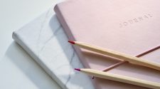 Minimalist self care journals in pastel pink and marble design with coloured pencils on a white desk, symbolising mindfulness, reflection, and wellbeing.