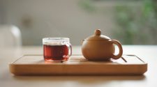 A steaming cup of herbal tea beside a ceramic teapot on a wooden tray, symbolising natural period pain relief and relaxation.