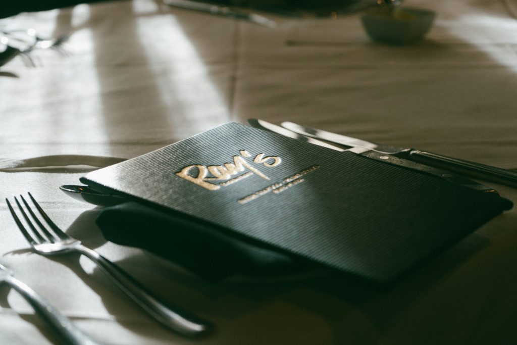 A close-up of a restaurant menu placed on a neatly set dining table with cutlery and soft natural light highlighting the elegant presentation.