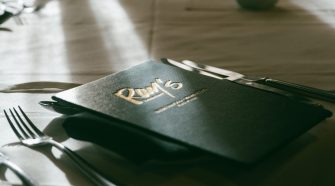 A close-up of a restaurant menu placed on a neatly set dining table with cutlery and soft natural light highlighting the elegant presentation.