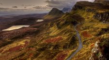A winding mountain road cutting through the dramatic, rugged landscape of the Quiraing on the Isle of Skye, with moody skies and rich autumnal colours across the hills.