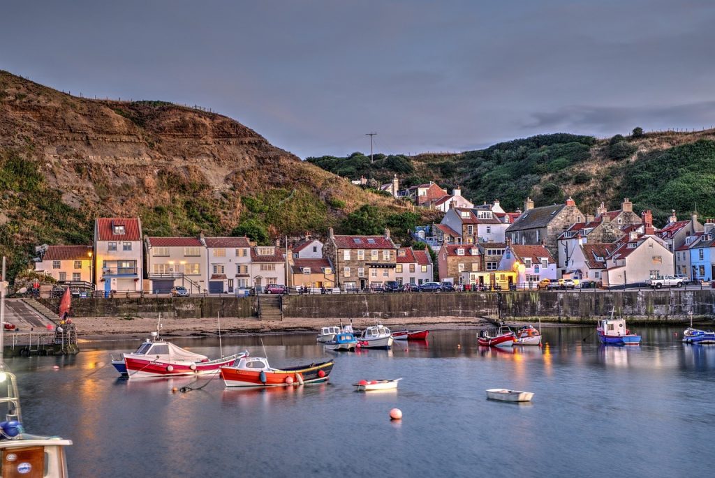 Picturesque view of Staithes harbour in North Yorkshire at dusk, with colourful fishing boats moored in calm water and traditional stone cottages nestled against the hillside.