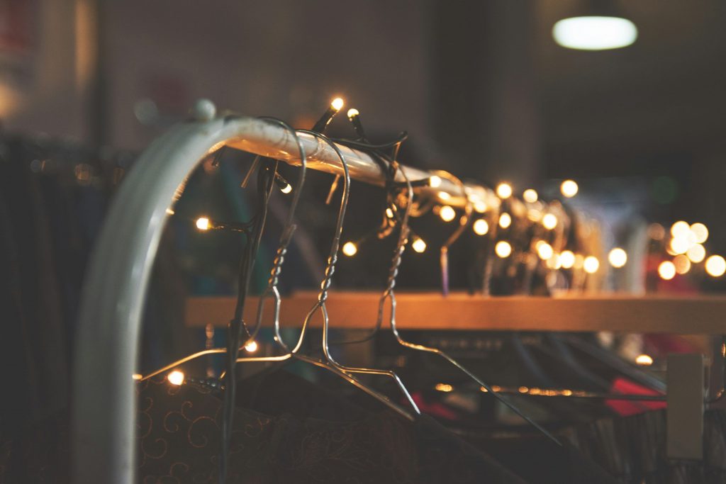 Clothing rail with metal hangers decorated with warm fairy lights in a softly lit, festive setting.