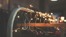 Clothing rail with metal hangers decorated with warm fairy lights in a softly lit, festive setting.