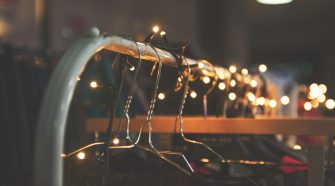 Clothing rail with metal hangers decorated with warm fairy lights in a softly lit, festive setting.