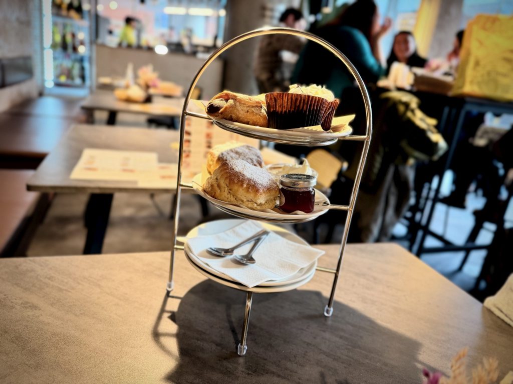 Three-tier afternoon tea stand on a café table at Nesso in Leeds, with scones, cakes and jam in the background.
