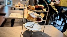 Three-tier afternoon tea stand on a café table at Nesso in Leeds, with scones, cakes and jam in the background.