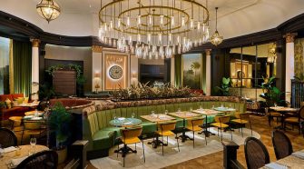 Interior of Cinnamon Kitchen Leeds at The Queens Hotel – a grand dining space with art deco chandeliers, curved green banquettes, and lush botanical accents