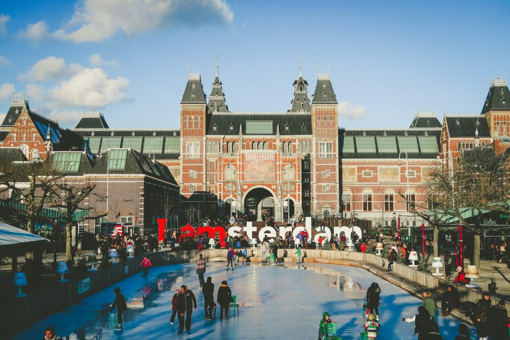 Winter scene in front of Amsterdam’s Rijksmuseum, with people skating on the ice rink and the “I amsterdam” sign in front of the grand brick façade.