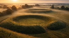 Sunrise over the Thornborough Henges in North Yorkshire, an ancient Neolithic site linked to Celtic mythology, surrounded by misty countryside and rolling fields.