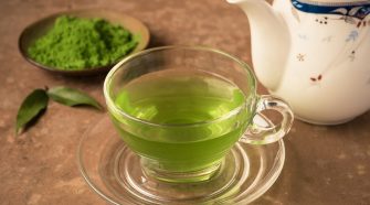 Glass cup of hot matcha green tea with matcha powder and teapot on a rustic surface