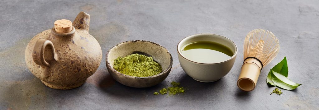 Traditional matcha tea set with bamboo whisk, ceramic bowl, matcha powder, and freshly prepared matcha green tea