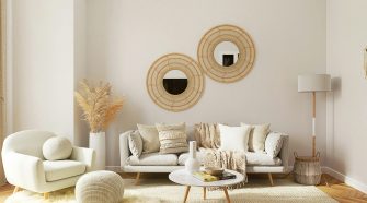 Light, neutral-toned living room with a beige sofa, textured cushions and throws, a matching armchair, woven wall mirrors, soft rug, wooden coffee table, and floor lamp, creating a calm and comfortable space.