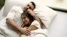 Couple sleeping peacefully in bed, cuddling under white bedding, illustrating comfort, closeness and a shared sleep setup.