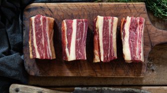 Raw bone-in beef short ribs on a wooden chopping board with visible marbling and thyme