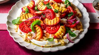 Grilled South African peach winter salad with tomatoes, labneh, fresh herbs and crisp flatbread served on a white platter.