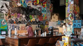 Alt text: Independent café interior with colourful street art walls, bar seating, and a staff member preparing drinks behind the counter, reflecting a modern, creative local dining space.
