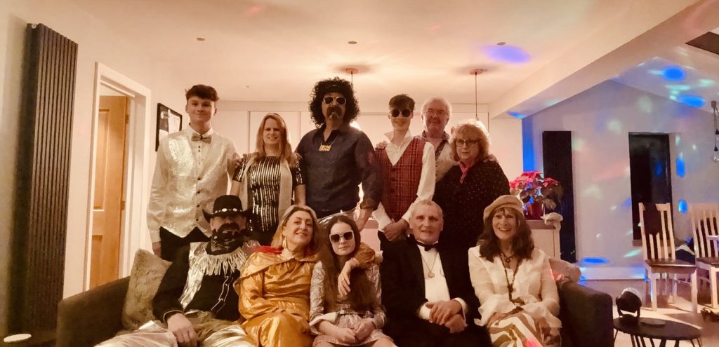Family and friends gathered in costume for a lively themed dinner party with disco lights and warm indoor setting