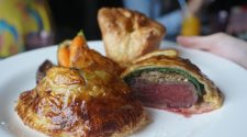 Individual beef Wellington parcels with golden puff pastry, one sliced open to reveal pink beef centre, served with roasted carrots and a Yorkshire pudding on a white plate.