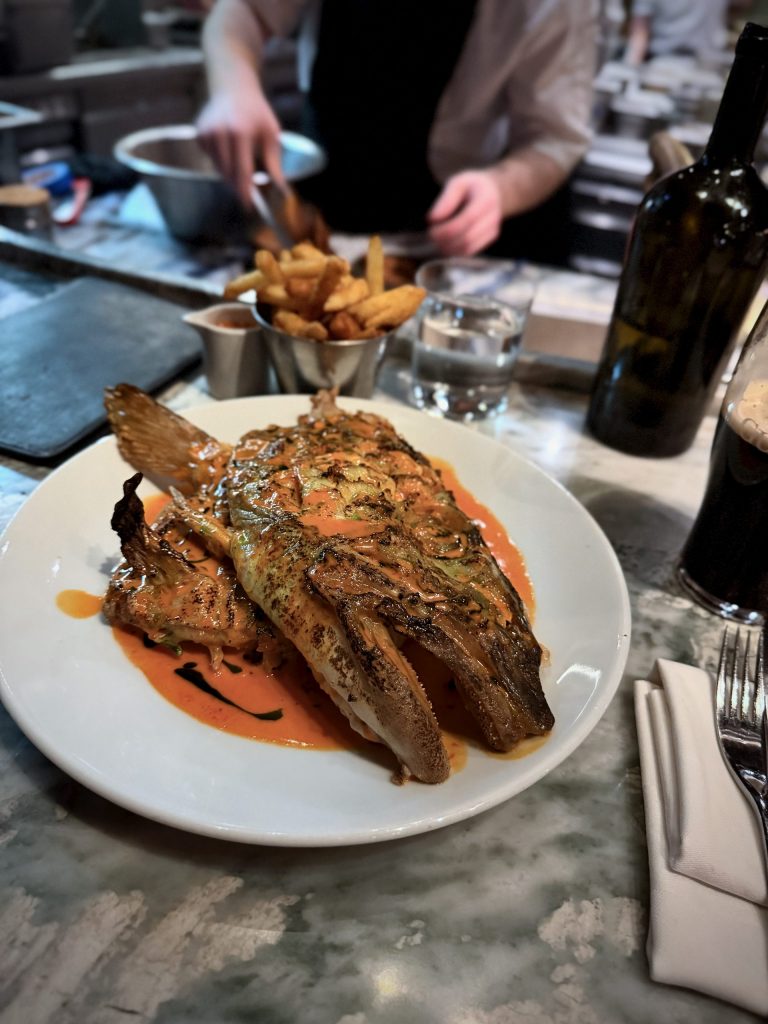 Fallow London smoked cod’s head served with sriracha sauce, plated at the chef’s counter with fries and kitchen action in the background