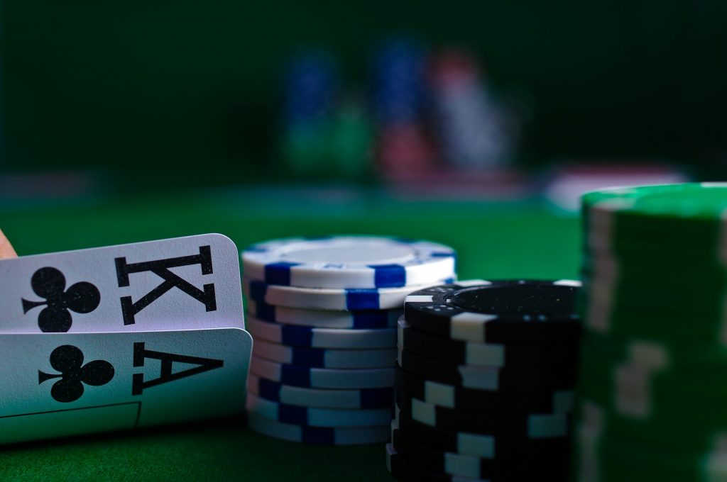 Poker chips stacked on a green casino table beside two playing cards showing the king and ace of clubs, with blurred chips in the background.