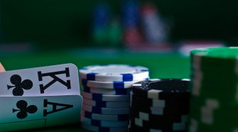 Poker chips stacked on a green casino table beside two playing cards showing the king and ace of clubs, with blurred chips in the background.